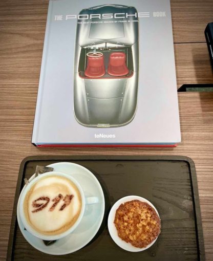 Cup of coffee with 911 dusted onto its milk foam with a picture book of Porsche 911 next to it.