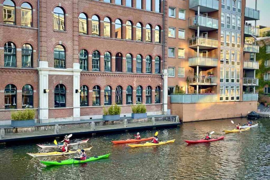 Group of colourful kayaks rolling along a canal in front of a majestic building.