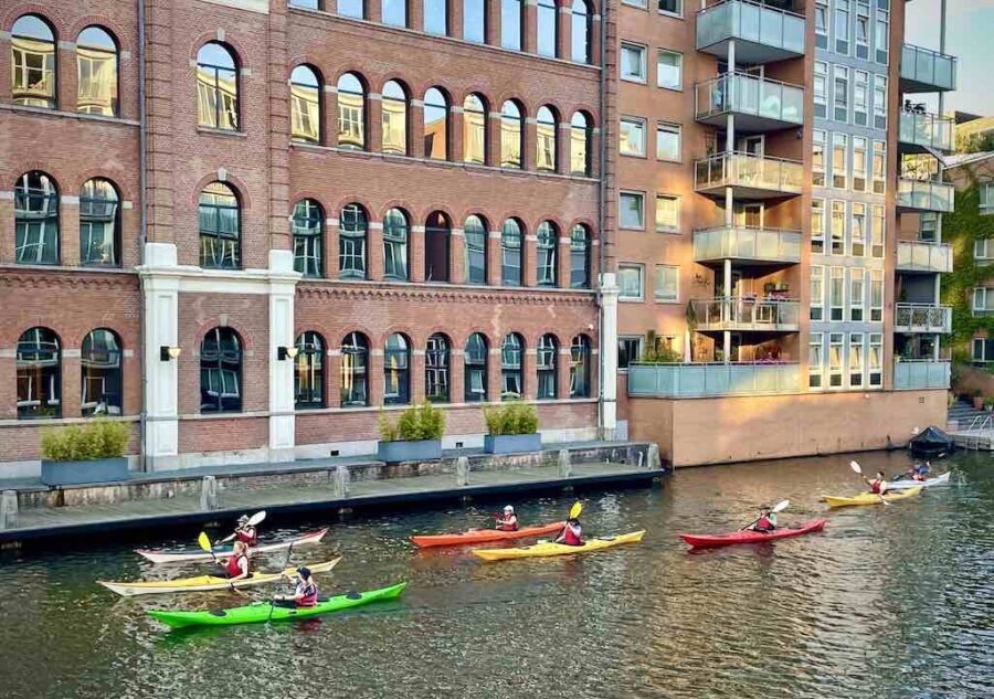 Group of colourful kayaks rolling along a canal in front of a majestic building.