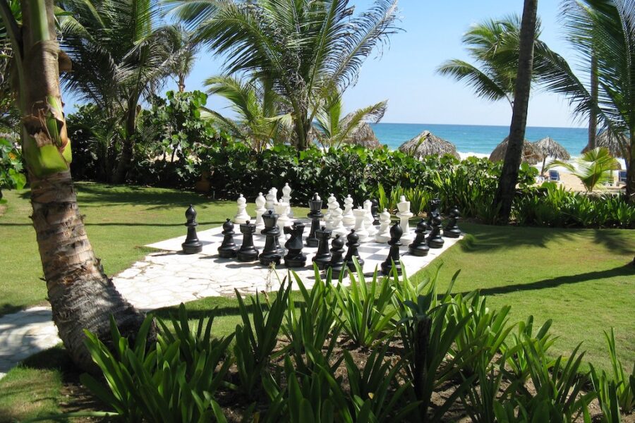 Huge chess pieces on a ground chessboard in front of beach.