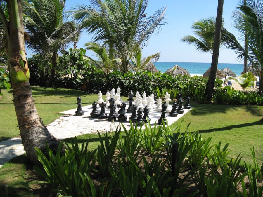 Huge chess pieces on a ground chessboard in front of beach.