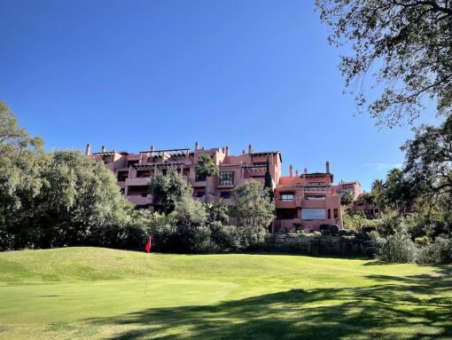 Golf green in front of salmon pink apartments.