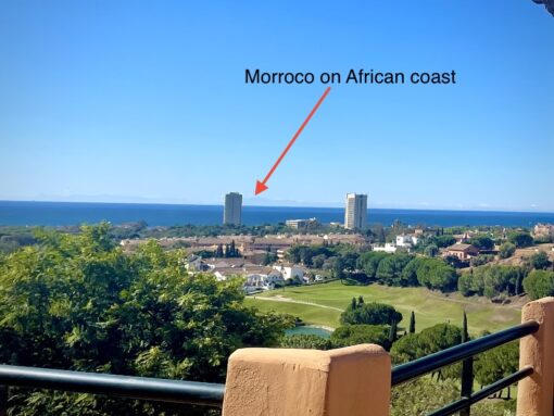 Balcony view of Atlas Mountains in Marbella, with golf course and Mediterranean Sea foreground. 