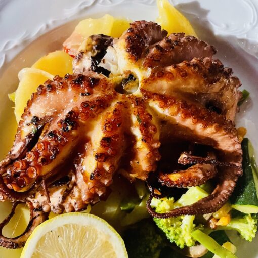 Grilled octopus dish on a bed of vegetable with a wedge of lemon at side.