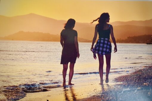 2 BFFs walking along the beach silhouetted against golden sunset.