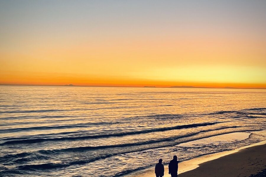 A couple walking along the beach during a golden sunset.