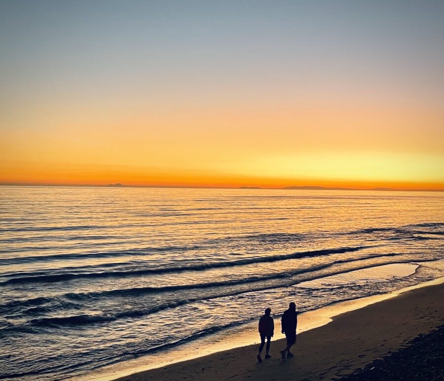 A couple walking along the beach during a golden sunset.