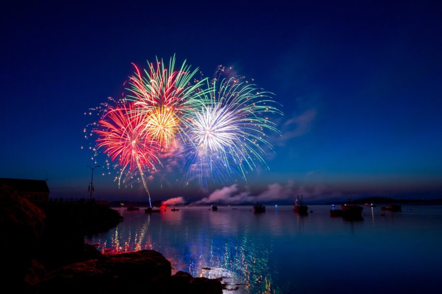 Burst of colourful fireworks lighting up a night sky above a lake.