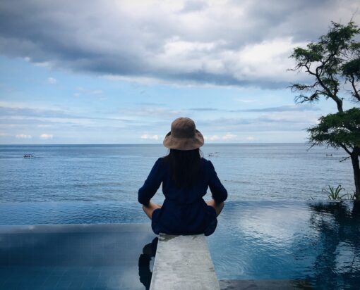 Female figure in meditation pose in front of infinity pool overlooking the ocean.