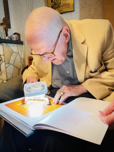 Shot of an elderly man reading a book under a magnifying class. 