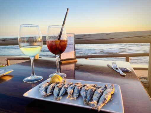 2 glasses of wine and a plate of sardines on table with direct sunset sea view.