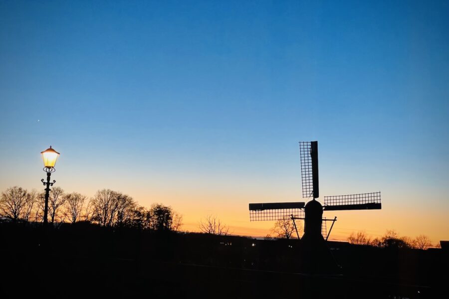 Windmill silhouette next to street lamp during sunset.