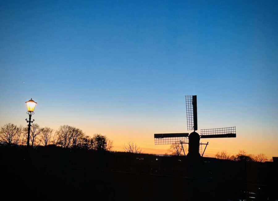 Windmill silhouette next to street lamp during sunset.