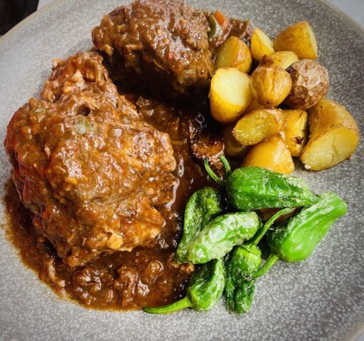 Delectable dish of oxtail stew with bud potatoes and padrón peppers. 