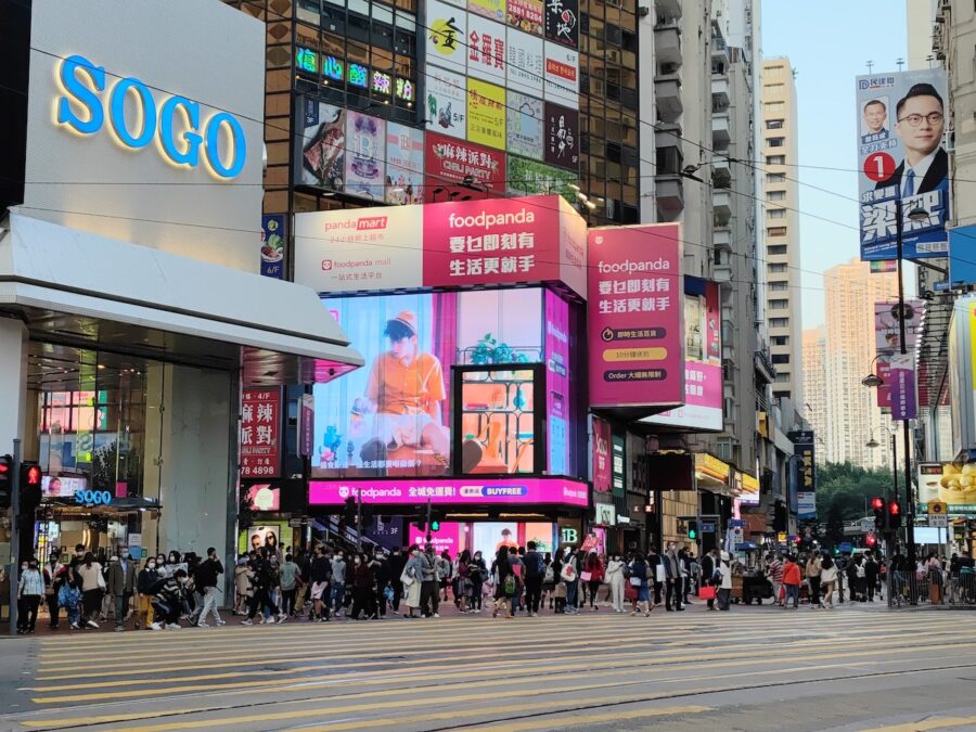 Busy street in Hong Kong teeming with pedestrians below gigantic advertising signboards.