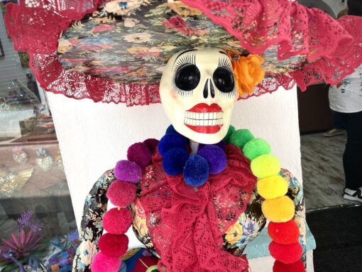 Skeleton dressed in wide-brimmed hat, colourful necklace and embroidered blouse with painted red lips.