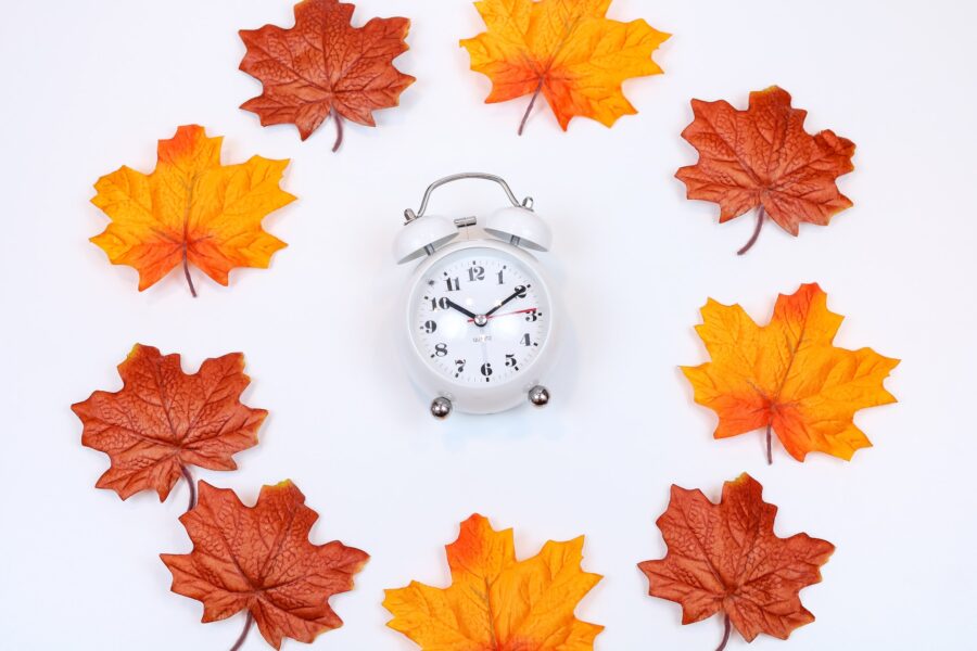 Old fashioned alarm clock encircled by red and orange maple leaves.