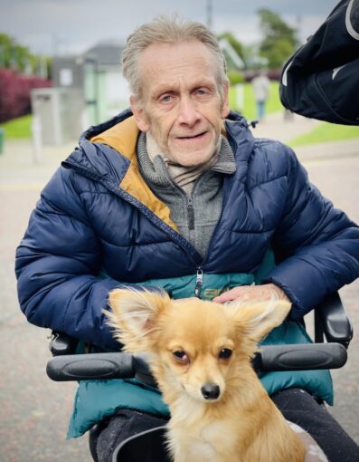 Elderly man in wheelchair with his dog in front.