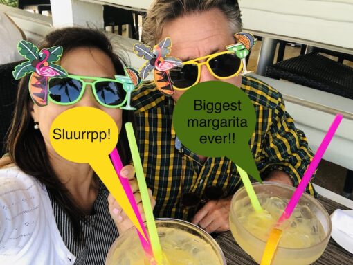 Couple slurping on giant margarita cocktails donning funny sunglasses.