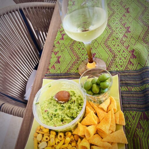 Glass of wine with a serving of nuts, olives and crackers with guacamole dip.