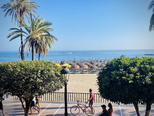 Paseo Maritime in Marbella Old Town bustling with cyclists, joggers, strollers and sun lounges on the beach and water craft in the ocean. 