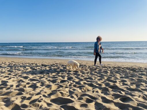 Woman walking her puppy on a beach.