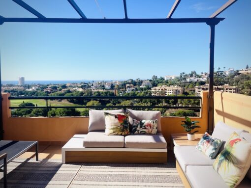 Sunny balcony with cosy furniture and amazing view of golf club and ocean in the background. 