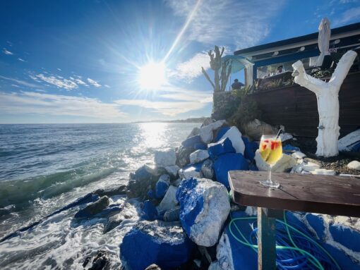 Glass of cocktail purged on a table at the edge of a bar on the beach.