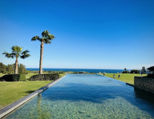 Reflective pool in the middle of golf fairway flanked by palm trees and putting green.