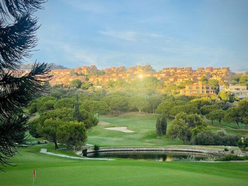 Golf course in a valley in front of a row of Andalucian apartments.