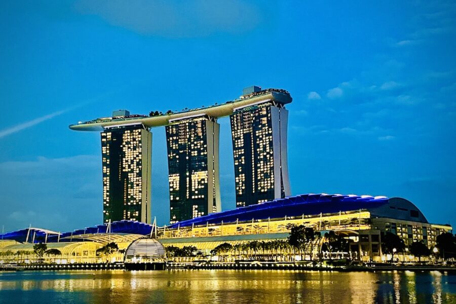 The iconic Singapore Marina Bay Sands with 3 towers linked by a 'boat' structure are the top, with lighted buildings below.
