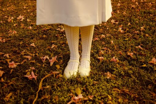 Lower bottom of woman in white skirt, socks and shoes standing a field.