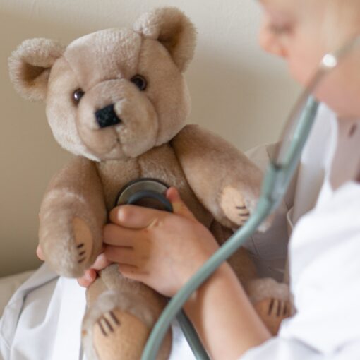 Young child listening through a stethiscope placed o a teddy bear's heart.