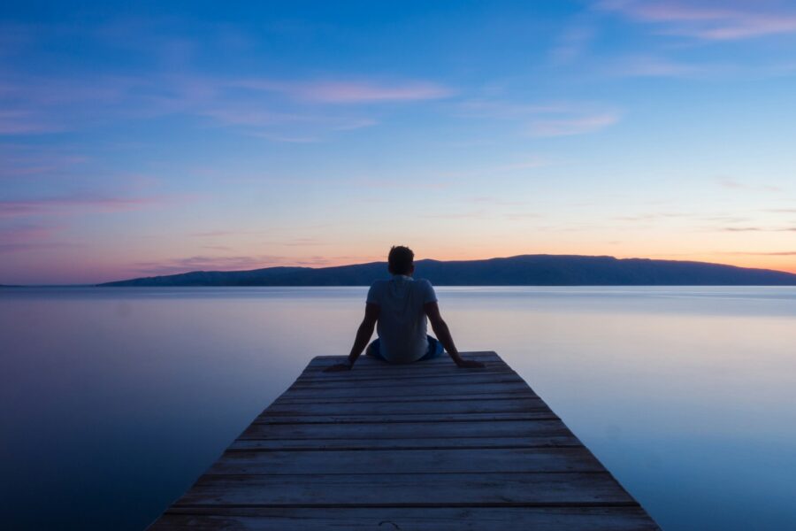 A man sitting at the edge of a jetty looking into the sea and sunset.