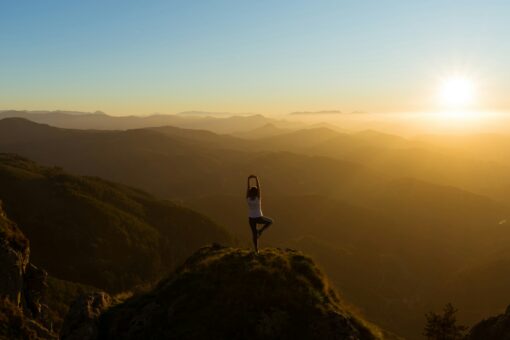 Solitary woman in a yogo pose on a mountain top at dawn.