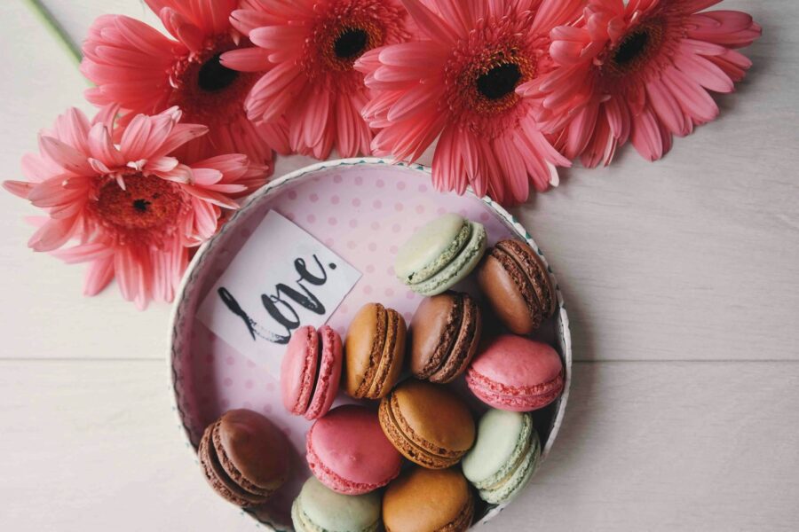 Plate of macarons with a scribbled 'love' note next to pink carnations.