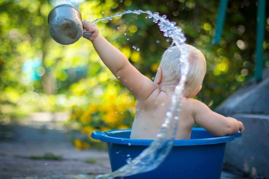 Baby playing with bath water in a tub in a garden.