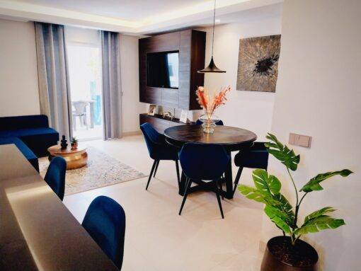 Interior of a luxuriously decorated apartment showing dining table with chairs and TV console. 