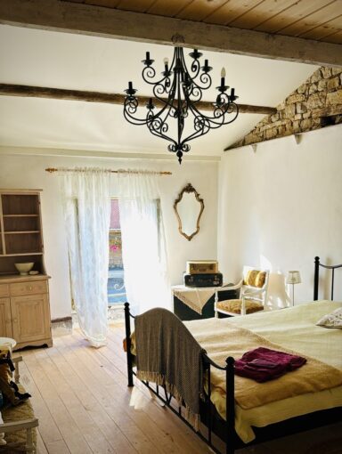 A cosy and rustic bedroom with chandelier and wrought-iron bed. 