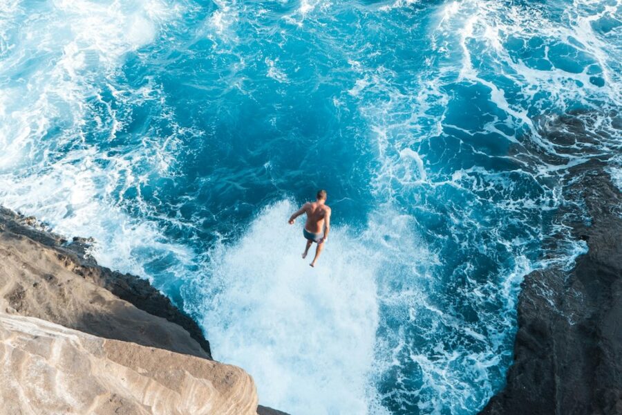 A man taking a huge jump from a cliff into slapping waters below.