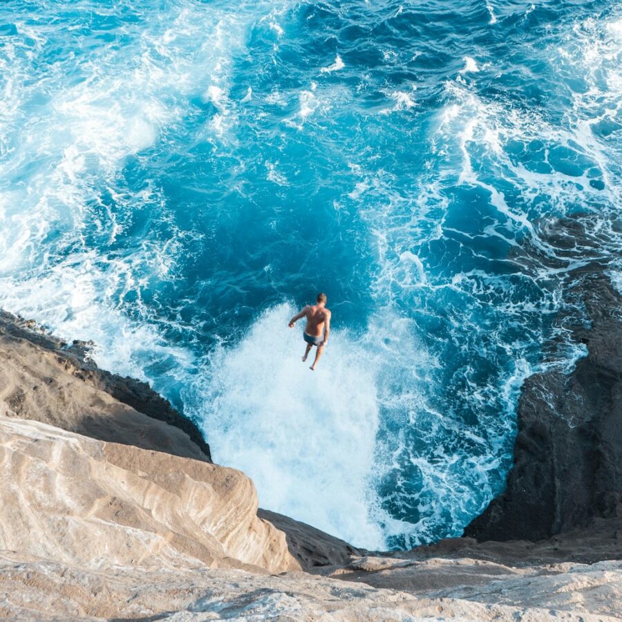 A man taking a huge jump from a cliff into slapping waters below.