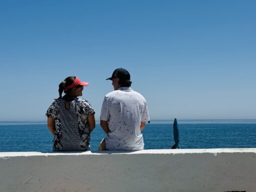 Photo of a couple sitting and chatting in front of calm ocean in midday.