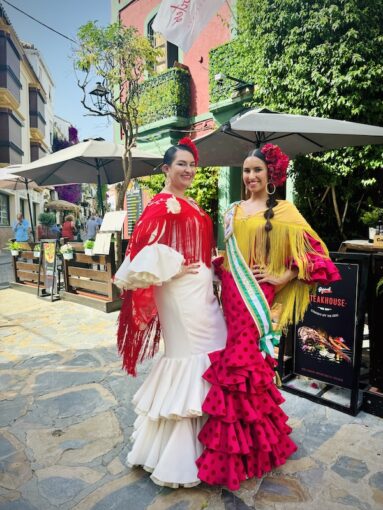 2 colourfully dressed women wearing traditional flamenco dresses posing on a Spanish street.