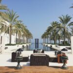 View of infinity pool with palm trees long both sides and lounge chairs.