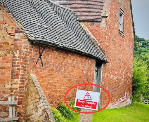 Back of a farm house with a sign "Dozy people on road" in front. 