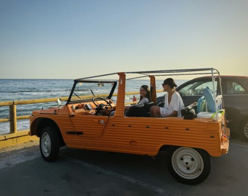 Orange Citroen Mehari with 2 women on board, at early sunset parked right in front of the beach.