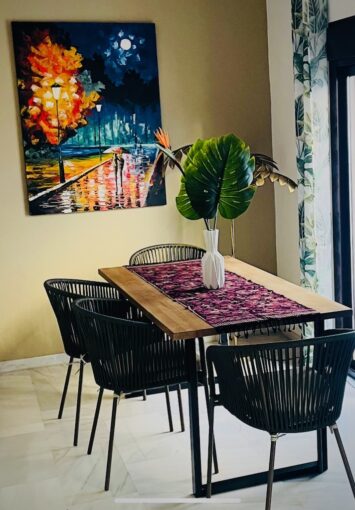 Warm cosy dining table with against a mustard colour wall with painting and a vase of leaves on it.