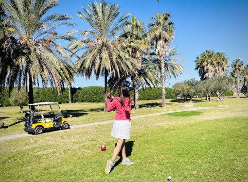 Woman in golf pose after hitting a driver from tee box with a buggy in the background. 