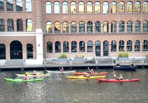 Colourful canoes along an Amsterdam canal with backdrop of a majestic building.