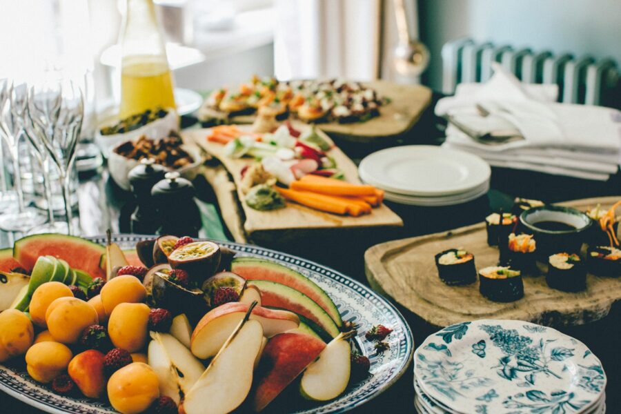 Table with spread of sushi, platter of cut fruit, dips, small bites amidst champagne glasses and dinner plates.